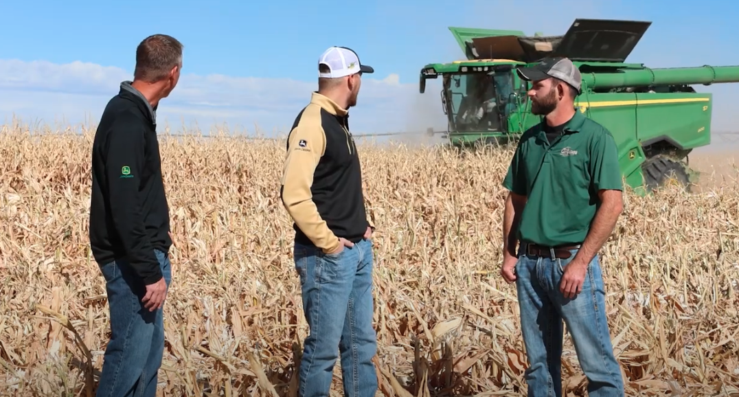 Mike, Preston, and Troy of the FarmCast look as an S7 Combine rolls through a cornfield behind them.